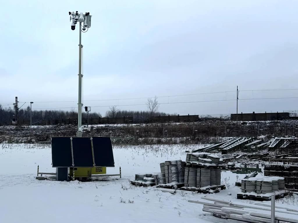 Mobile Videoüberwachung an einer Bahnbaustelle – solarautarker Überwachungsturm der Secura.Zone X-Line mit PTZ-Kameras im Wintereinsatz, Sicht über Schwellenstapel, Materiallager und Gleis mit Oberleitung Mobile Videoüberwachung an einer Bahnbaustelle – solarautarker Überwachungsturm der Secura.Zone X-Line mit PTZ-Kameras im Wintereinsatz, Sicht über Schwellenstapel, Materiallager und Gleis mit Oberleitung